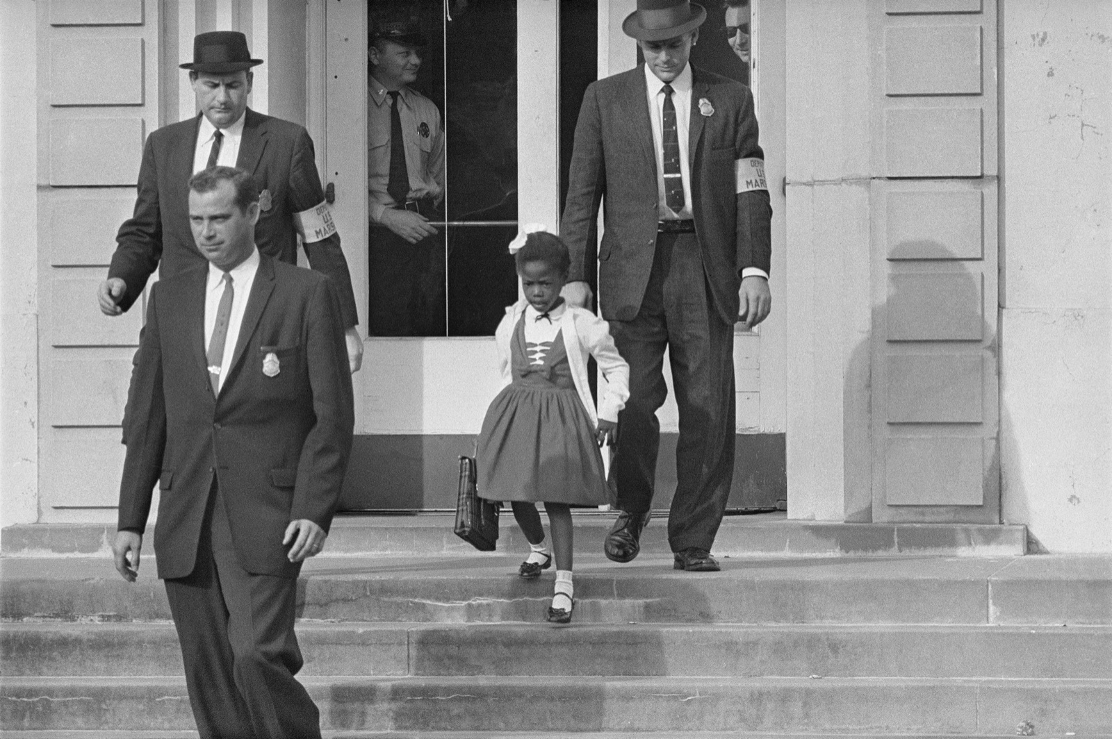 Ruby Bridges, age six, escorted down the steps of William Frantz Elementary School by four U.S. deputy marshals, New Orleans, November 14, 1960 — the real photograph Rockwell worked from