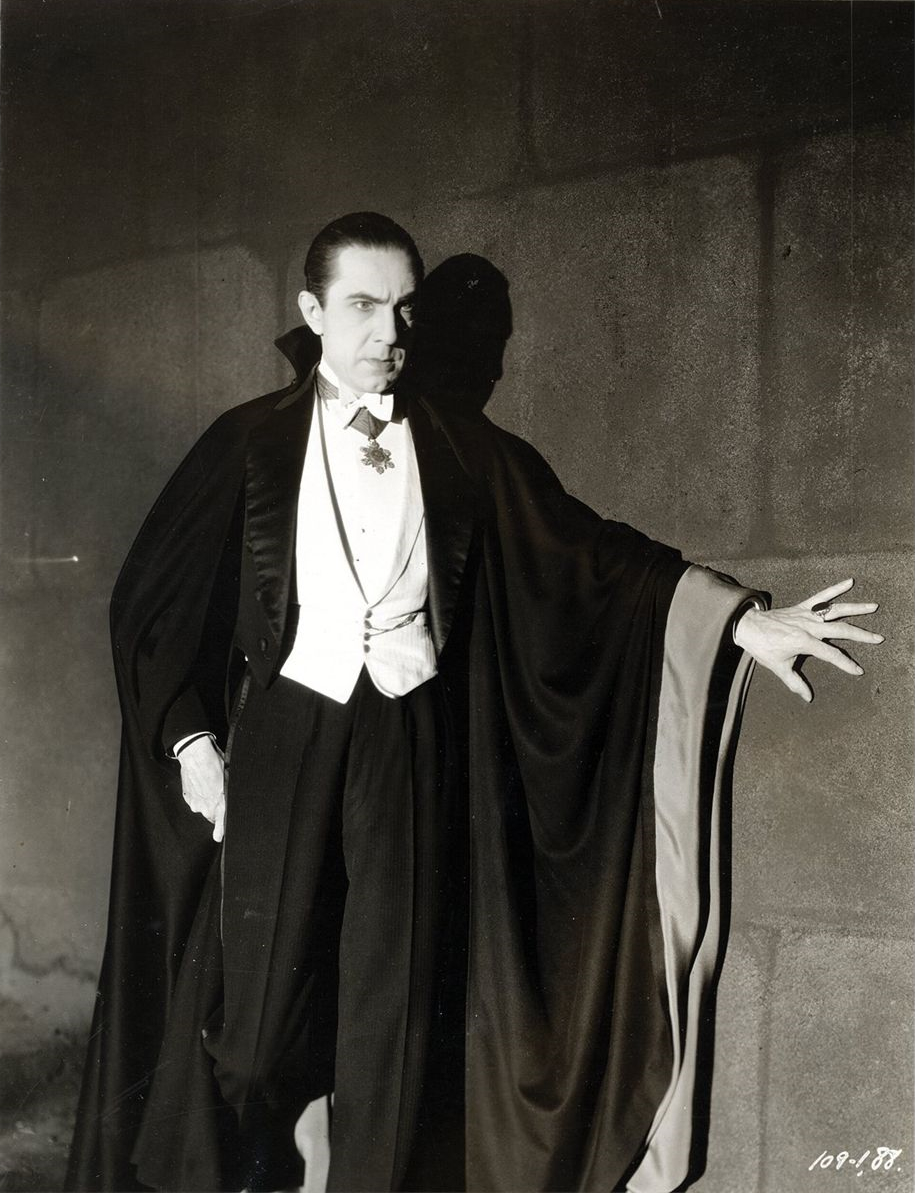Bela Lugosi as Count Dracula in a 1931 Universal publicity photograph, standing in the full black cape with its pale lining, one hand extended