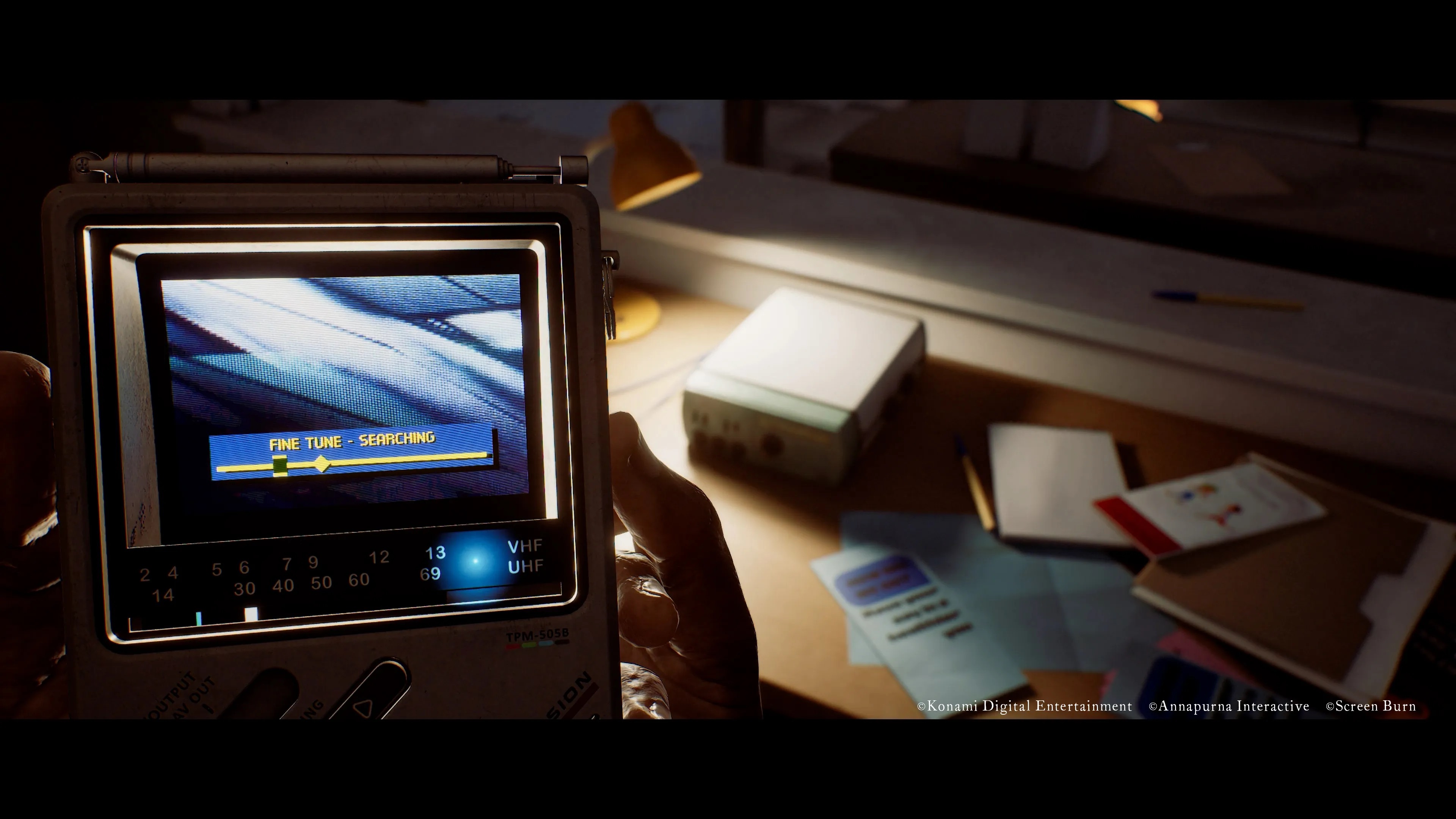A handheld analog TV tuner reading FINE TUNE - SEARCHING, held up in a dim room, from Silent Hill: Townfall