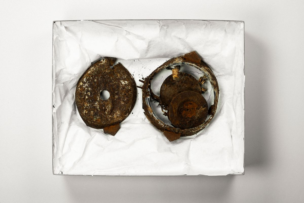 A badly rusted, broken waffle iron in two pieces, resting in an archival storage box