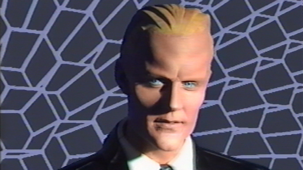 Close-up of Matt Frewer in the Max Headroom prosthetic makeup and blond wig, mid-performance against a geometric background