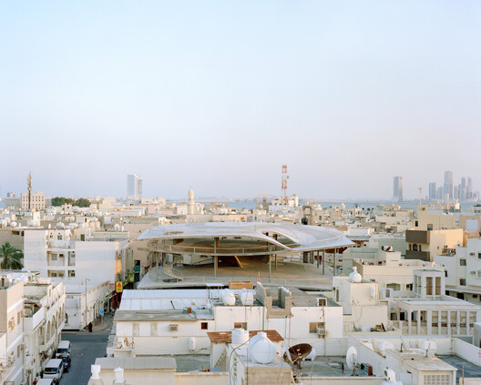 Aerial view of Muharraq's dense old town with one of Christian Kerez's sculptural car parks visible as a pale curved roof among the rooftops