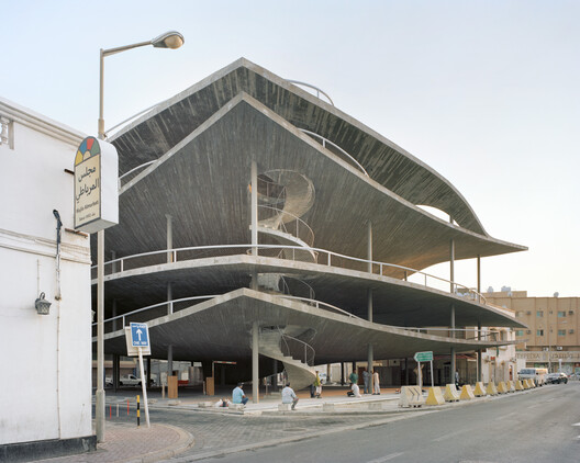 A sculptural multi-level concrete car park in Muharraq, Bahrain, with sloping continuous ramps and a spiral stair, photographed at dusk