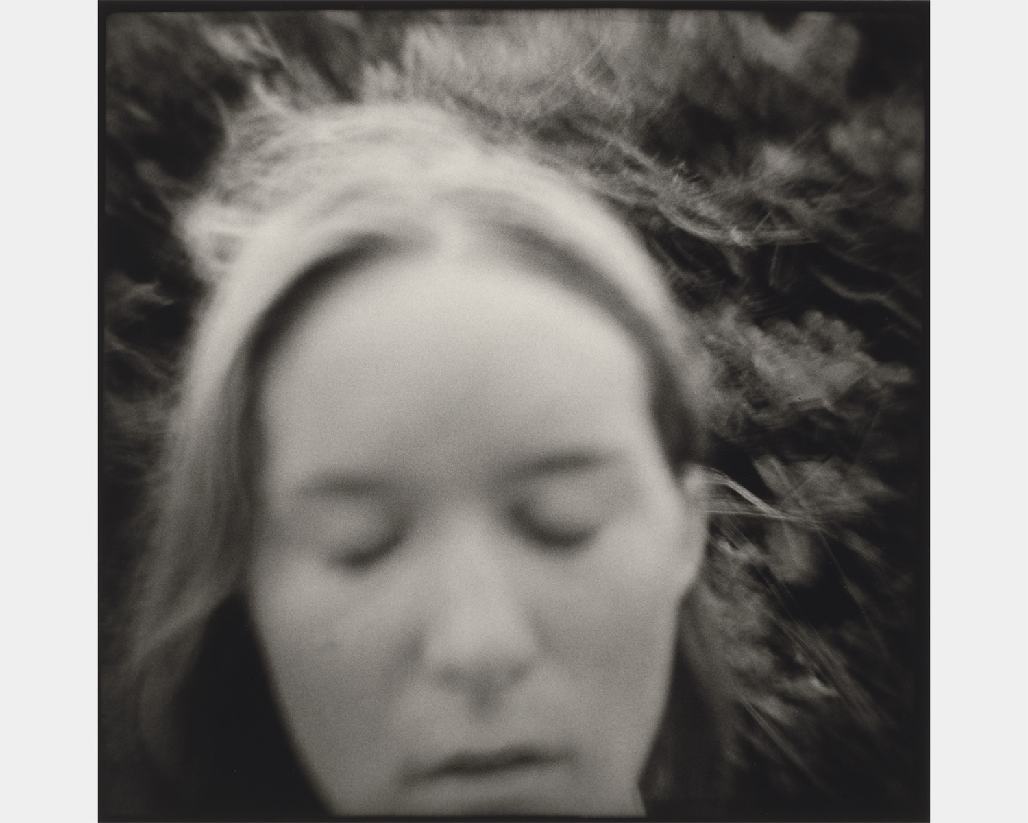 A blurred black-and-white self-portrait: a woman's face with closed eyes and a hairband, soft focus and dark vignetting around the frame