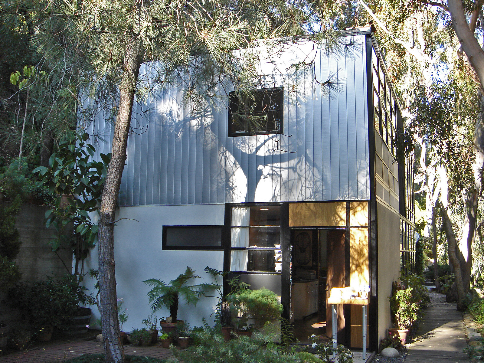 The studio building of the Eames House, a two-storey box with aluminium cladding and black steel frames, open door at ground level