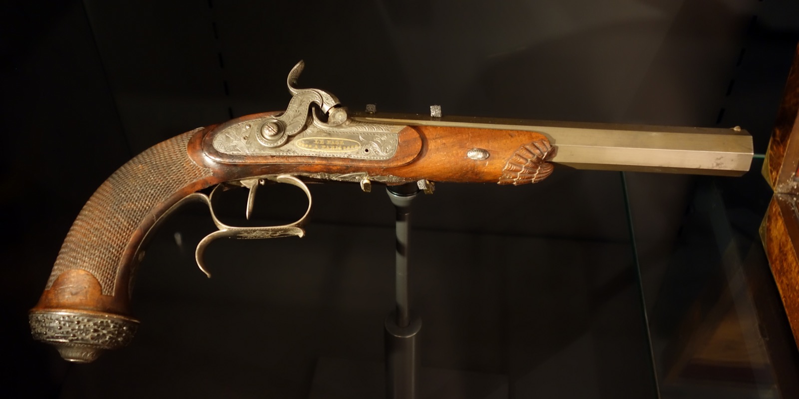 A percussion duelling pistol with an octagonal barrel and engraved silver lock plate reading Le Page, in a museum case