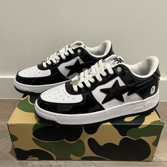 A pair of black and white patent leather Bape Sta sneakers with star logos, sitting on a green camo shoebox