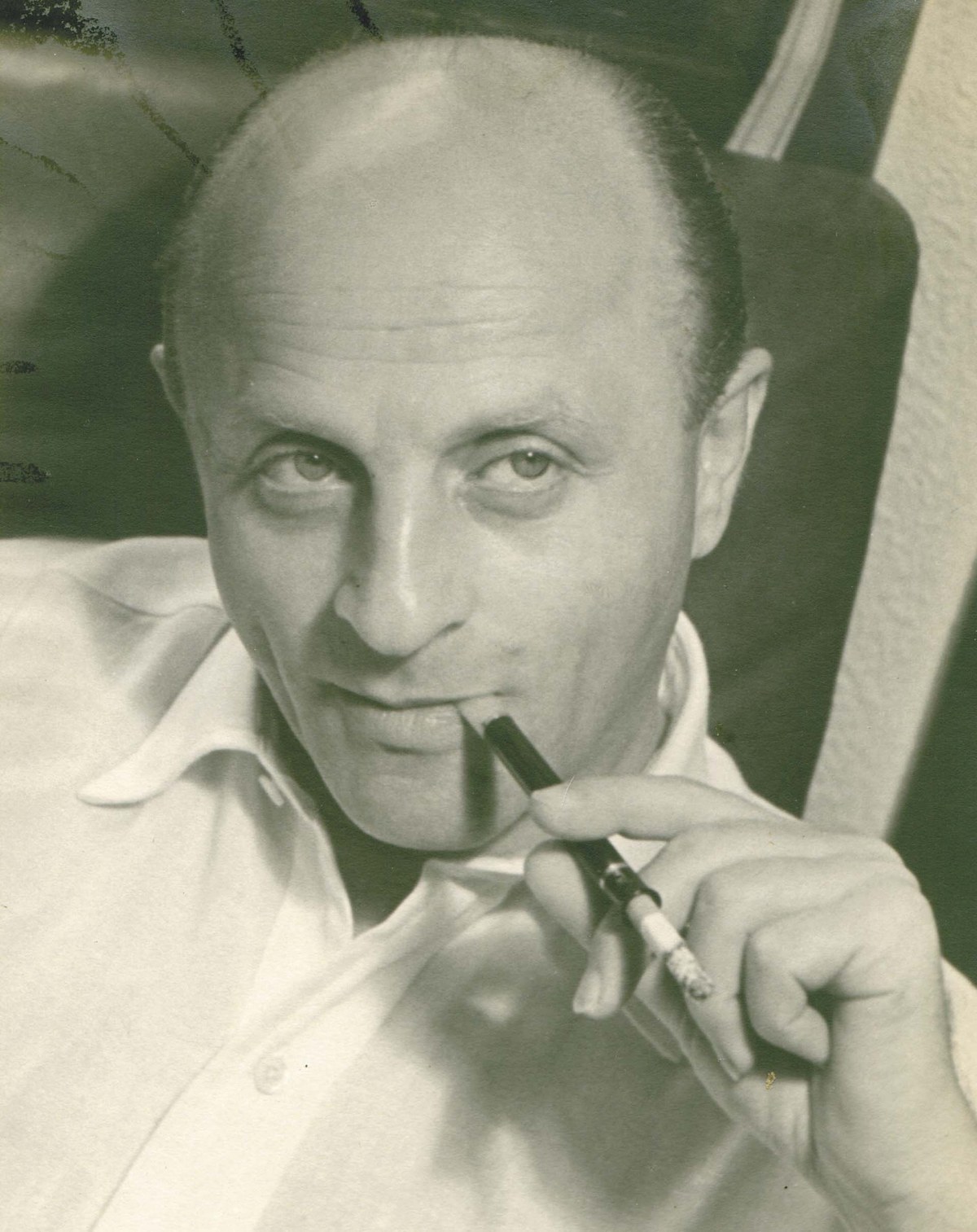Black and white portrait of a balding man smiling slightly, holding a pen to his lips